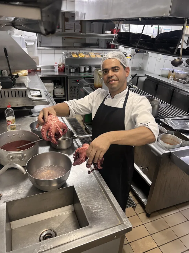 Cozinheiro do Grupo Insalata sorrindo enquanto prepara polvo na cozinha