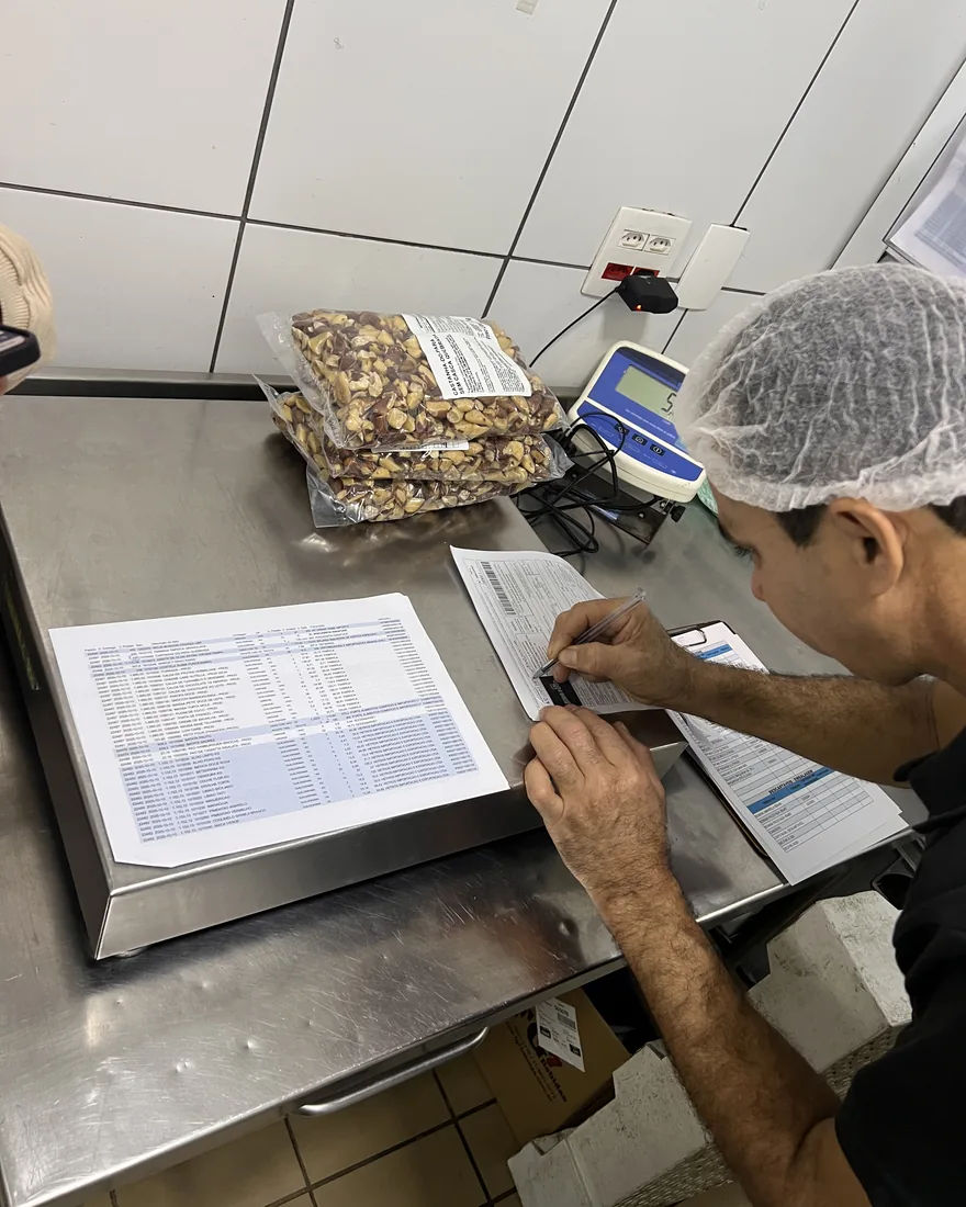 Operador do Grupo Insalata conferindo um recebimento na balança, com nota fiscal e sacos de castanha